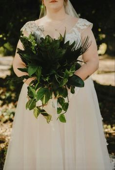 a woman in a wedding dress holding a bouquet of greenery and looking at the camera