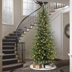 a christmas tree in the middle of a room with presents on the floor and stairs