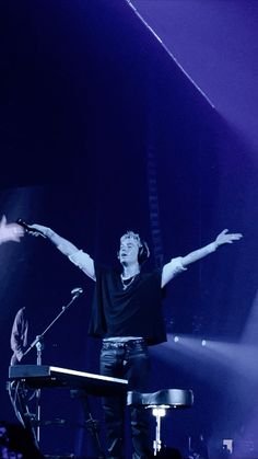 a man standing in front of a keyboard on stage with his arms spread wide open