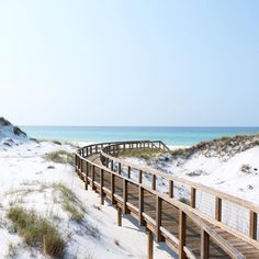 a wooden walkway leading to the beach with sand dunes in the background and grass on either side