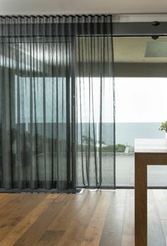 an empty room with wooden floors and sheer curtains on the window sill, looking out onto the ocean