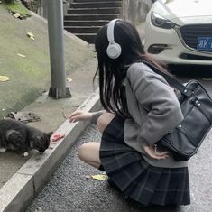 a woman kneeling down next to a black and white cat with headphones on her ears