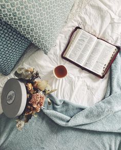 an open book, cup of coffee and flower on top of a bed with blue sheets