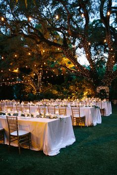 an outdoor dining area with tables and chairs covered in white linens, lit by fairy lights