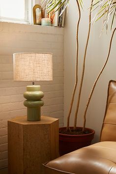 a green lamp sitting on top of a table next to a brown chair and potted plant