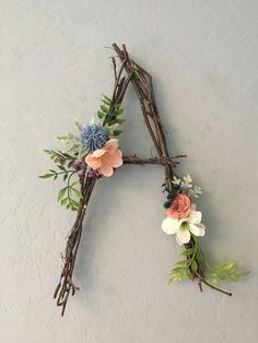 a letter made out of twigs with flowers and leaves on it's sides, hanging from the wall