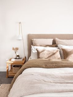 a bed with pillows and blankets on top of it next to a night stand in a bedroom