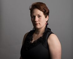 a woman with red hair and black dress posing for a photo in front of a gray background