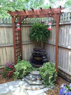 a small garden area with a fountain and flowers in the back yard, surrounded by wooden fence