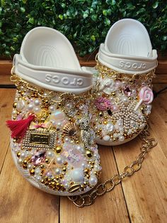 a pair of white slippers with lots of beads and charms on them sitting on top of a wooden floor