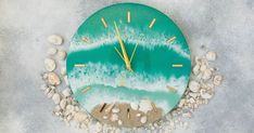 a clock that is on the side of a wall next to rocks and sand with shells around it