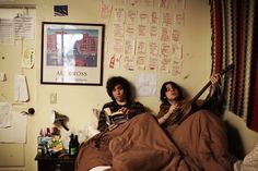 two people laying in bed reading books and looking at something on the wall above them