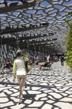 a woman walking down a walkway under a metal structure