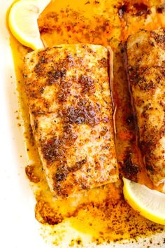 two fish fillets with lemon slices and seasoning on the side, ready to be eaten