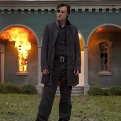 a man standing in front of a house with flames coming out of the building behind him