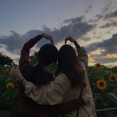 two people are standing in the middle of a field with sunflowers at sunset