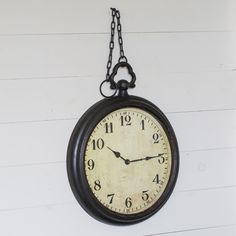 an old clock hanging from a chain on the wall with white walls in the background