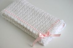 a white crochet baby blanket with pink ribbon on the end, sitting on a table