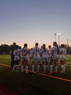 a group of women's soccer players huddle together on the field at sunset