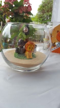 a glass bowl filled with miniature animals on top of a white tablecloth covered table