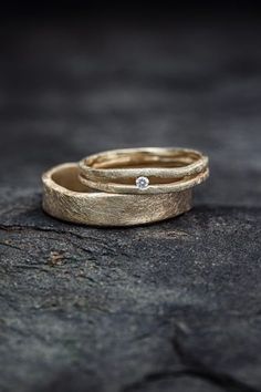 two gold wedding bands with diamonds on them sitting on a piece of rock in the sun