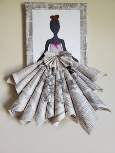 an origami dress made out of newspaper strips hanging on the wall above a framed art piece