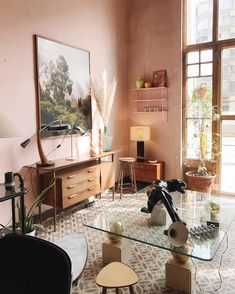 a living room filled with furniture and a painting on the wall above it's glass top coffee table