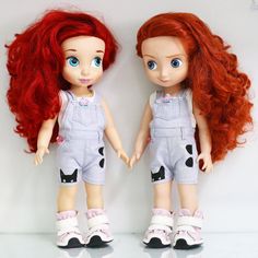 two dolls standing next to each other on a white surface with red hair and blue eyes