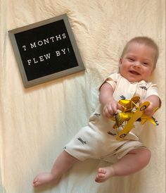 a baby is holding a yellow toy and smiling at the camera while laying on a bed