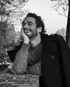 black and white photograph of a smiling man leaning on a tree trunk with his hand to his face