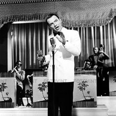 a man standing in front of a microphone while wearing a white jacket and black pants