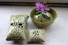 two pieces of pottery sitting next to a bowl with a purple flower in it on a table