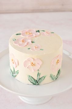 a white cake with pink flowers painted on the side and green leaves in the middle