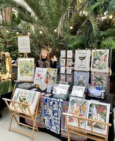 a woman is standing in front of some art on display at an outdoor market stall