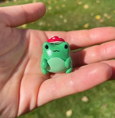 a small green frog with a red hat on it's head sitting in someones hand