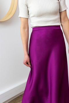 a woman wearing a white top and purple skirt