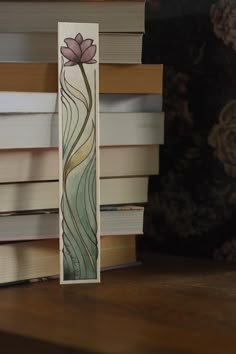 a bookmark made out of stained glass with a pink flower on it sitting in front of a stack of books