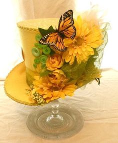 there is a yellow hat with flowers and a butterfly on the top, sitting on a glass plate