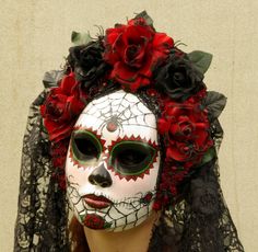 a woman wearing a white mask with red flowers on her head and black veil over her face