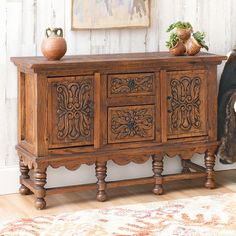 an old wooden sideboard with carvings on the doors and drawers, in front of a rug