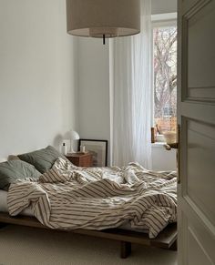 an unmade bed in a bedroom with a lamp hanging over the headboard and window