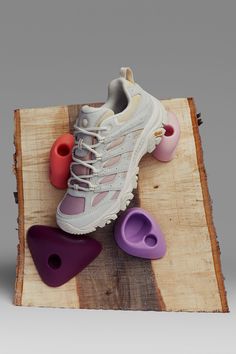 a pair of white sneakers sitting on top of a wooden board next to purple and red shoes