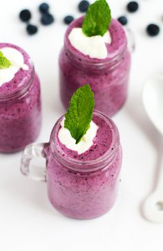 three glasses filled with blueberry smoothie and topped with whipped cream, green leaf