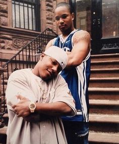 two men standing next to each other in front of some stairs and steps with their arms crossed