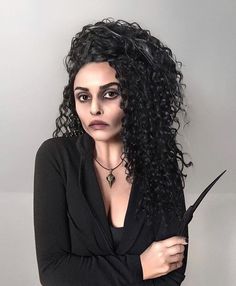 a woman with long curly hair is holding a knife in her hand and looking at the camera