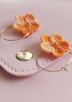 two small crocheted flowers are attached to gold hoop earrings on a pink surface