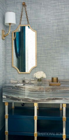 a bathroom with a marble counter top and gold accents on the mirror, along with a blue cabinet