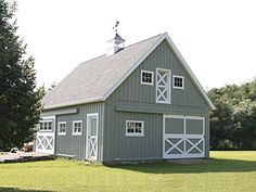 a large gray barn sitting in the middle of a lush green field next to trees