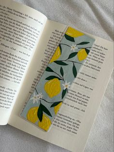 a bookmark with lemons and flowers on it sitting next to an open book