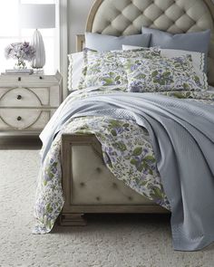 a bed with blue sheets and pillows in a bedroom next to a dresser, mirror and lamp